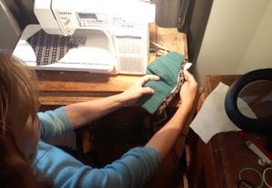 woman sitting by sewing machine holding up a mask