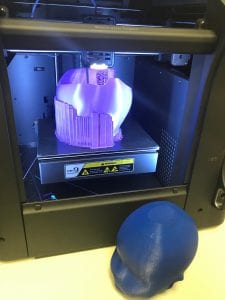 A baby helmet (cranial band) in the midst of being printed and a 3D-printed model head beside. 