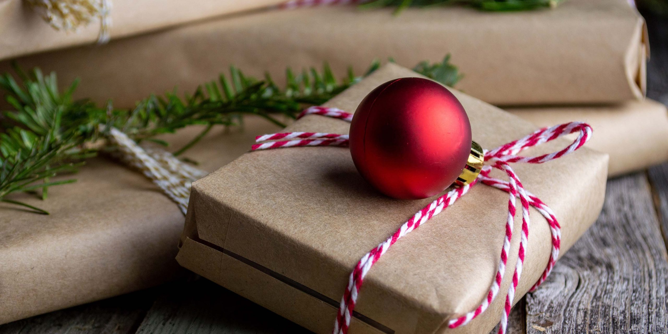 holiday gifts wrapped under a tree with a red ornament on top