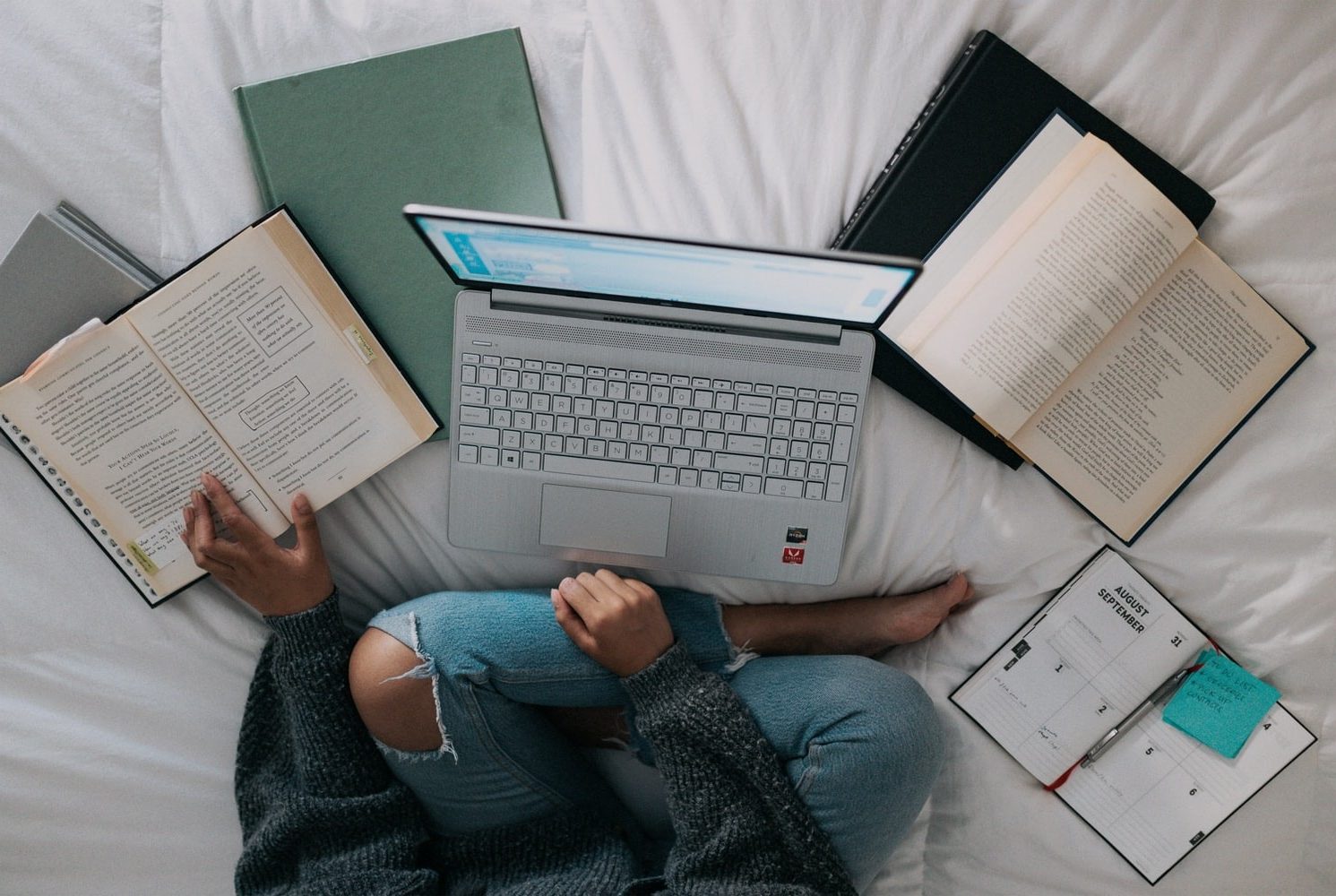 A student studying with a laptop and notebooks on a bed.