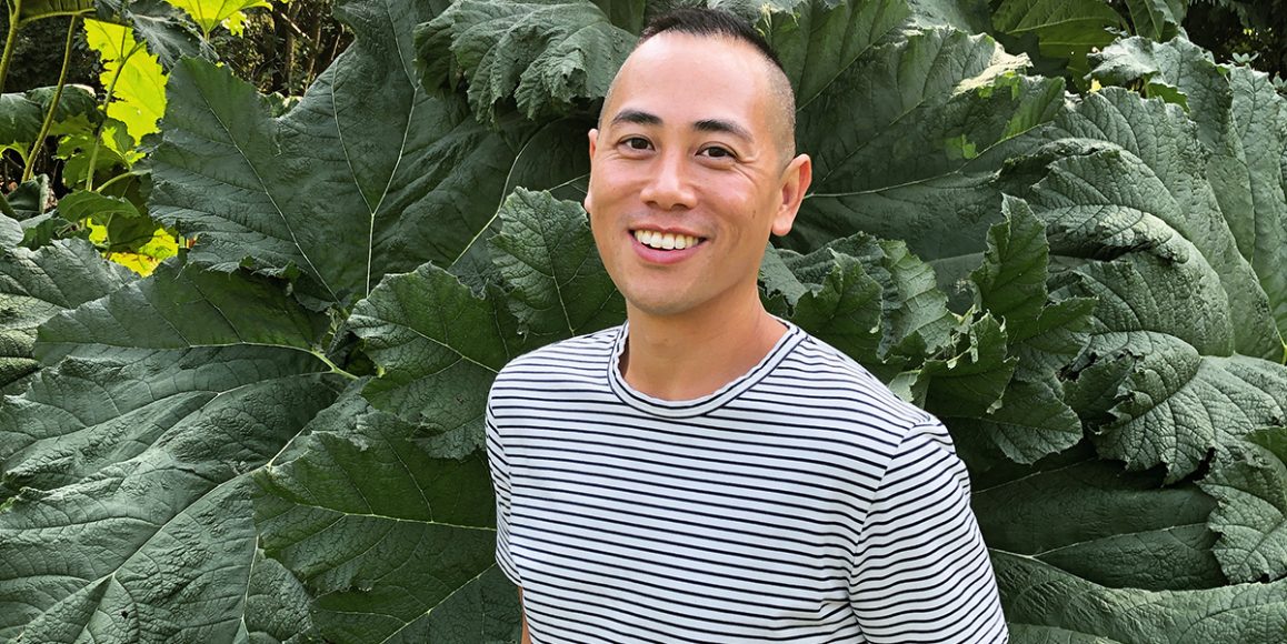 Eddy Boudel Tan smiling in striped t-shirt against backdrop of greenery