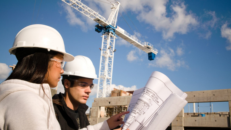 Two construction students discussing with each other, with a white crane in the background.