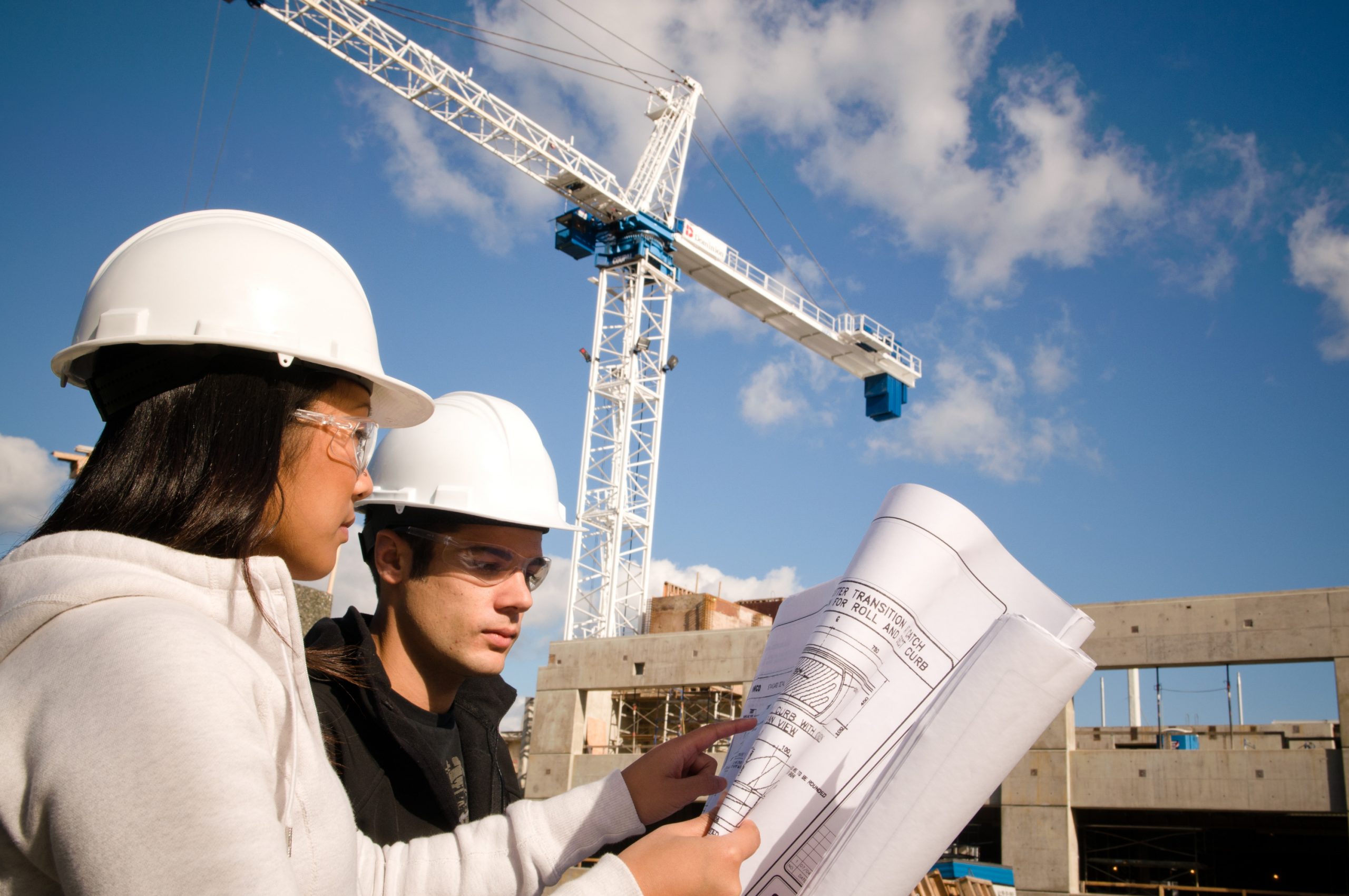 Two construction students discussing with each other, with a white crane in the background.