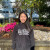 A picture of Joey in a black BCIT hoodie, in front of a colorful plant bed behind her.