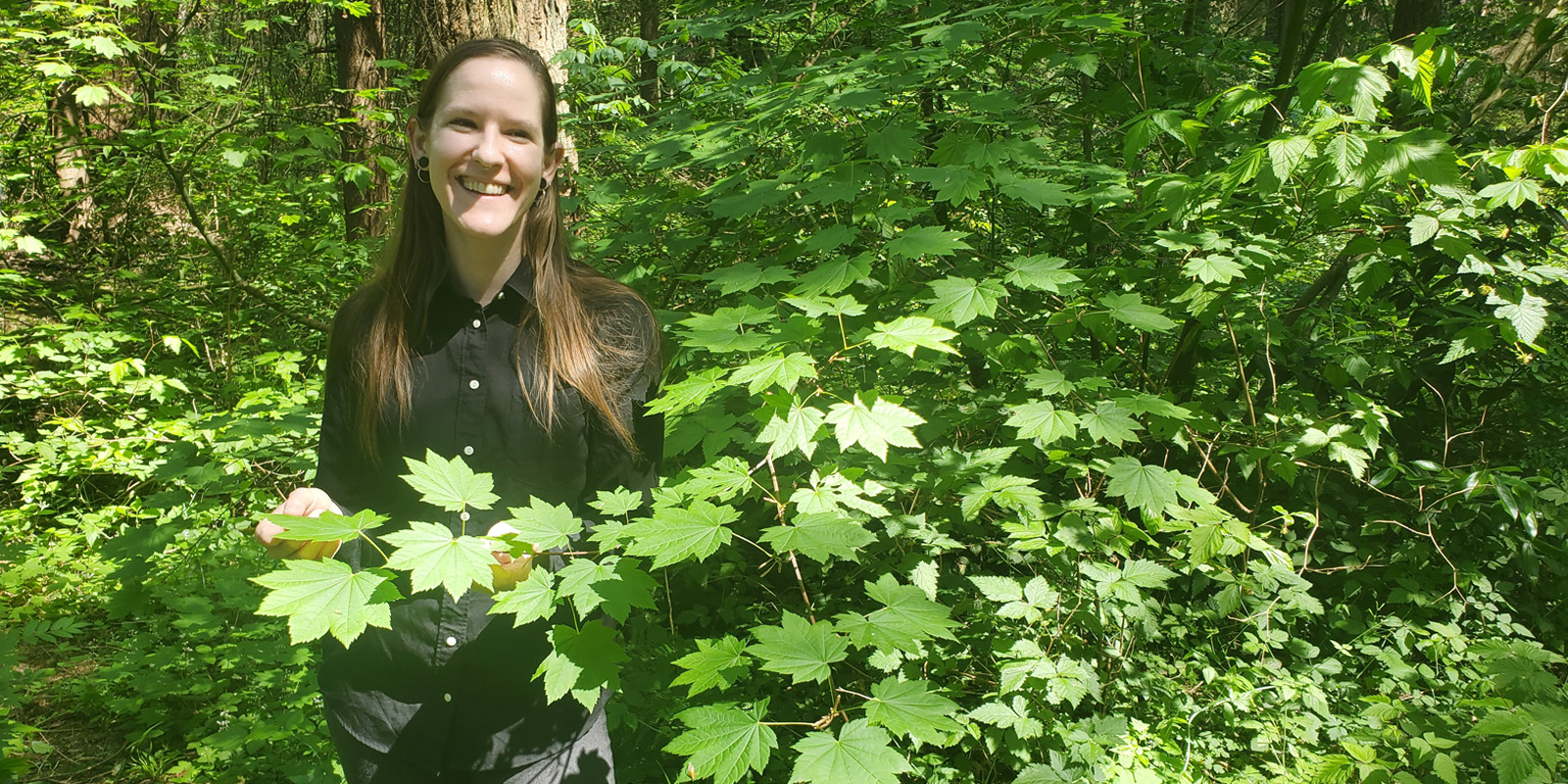 Erin Rutherford smiles surrounded by green leaves in a natural landscape, wearing all black