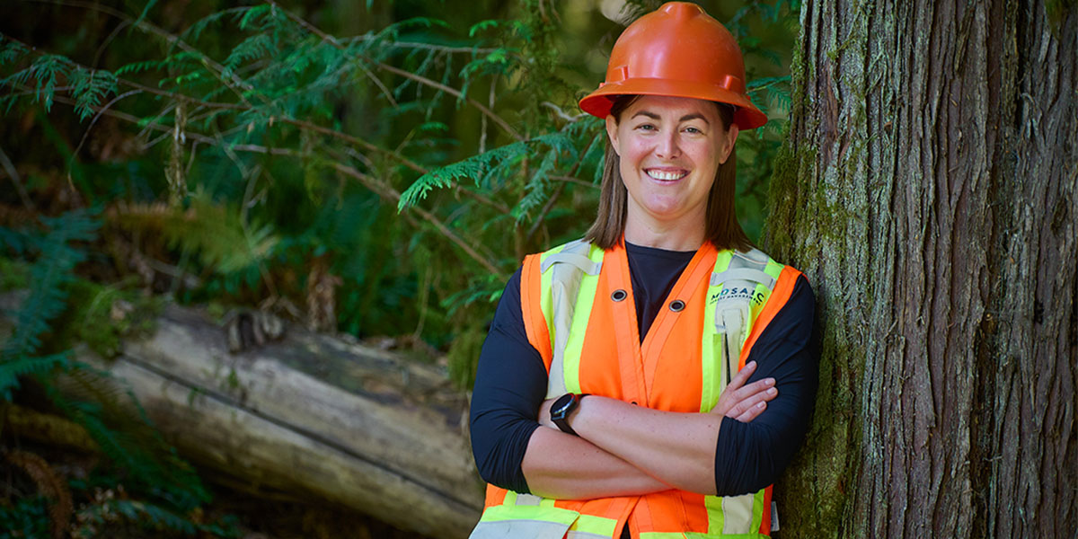 bcit alumna molly hudson poses in hard hat and vest in forest