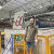 Man in his 40s with beard stands in a high tech industrial physics particle accelerator facility with the word Alpha behind him.