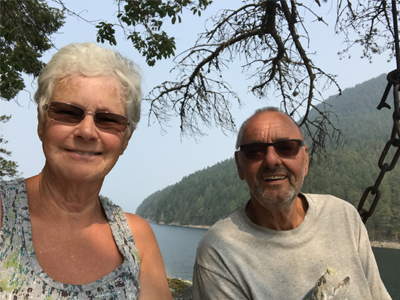 Peggy and Jim Waldbauer smiling in front of water and a mountain