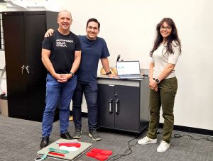 3 people standing in front a computer on a cart