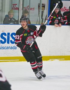 Matthew Cox in black and red hockey jersey changing direction while skating on ice, stick raised