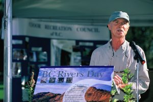 Mr. Angelo delivers a speech to celebrate BC Rivers Day in 2016. A sign in the foreground reads "BC Rivers Day"