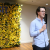 Matt Cox delivers a speech at the BCIT 2024 Spring Convocation Graduating Awards Ceremony. He holds a microphone, and stands in front of a yellow flower wall with a sign on it that reads "BCIT"