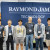 six men of a range of ages and backgrounds stand in front of a banner that reads "Raymond James Technology"